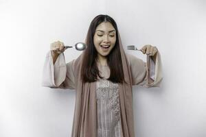 An Asian Muslim woman is fasting and hungry and holding cutlery while looking aside thinking about what to eat photo