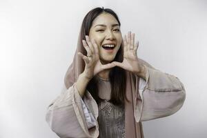 Young beautiful Asian Muslim woman wearing a headscarf shouting and screaming loud with a hand on her mouth. communication concept. photo