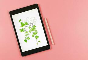 flat lay of digital tablet with picture of house plant in watercolor style on screen,  pink stylus pen,   isolated on pink  background. Digital art concept. photo
