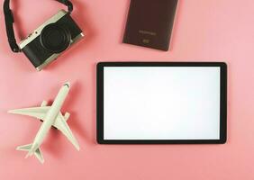 flat lay of digital tablet with blank white screen, airplane model, passport and digital camera isolated on pink background. travel planning concept. photo