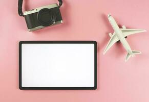flat lay of digital tablet with blank white screen, airplane model and digital camera isolated on pink background. travel planning concept. photo