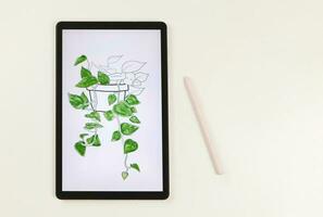 flat lay of digital tablet with picture of house plant in watercolor style on screen,  pink stylus pen,   isolated on white background. Digital art concept. photo