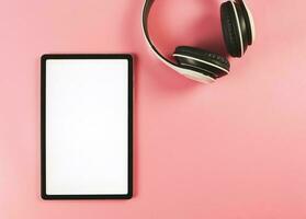 plano laico de digital tableta con blanco blanco pantalla y auriculares aislado en rosado antecedentes. foto