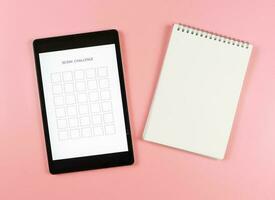 plano laico de digital tableta con modelo 30 día desafío en pantalla, abrió blanco página cuaderno aislado en rosado antecedentes. foto