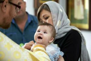 bielorrusia, el ciudad de gomel junio 15, 2020. ciudad iglesia. bautismo de el niño. madre sostiene el bebé en su brazos durante el bautismo ceremonia. adoptar un religión foto