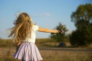 contento pequeño niña carreras en el prado con un ramo de flores de flores niño en un hermosa verano campo en contra el azul cielo. foto