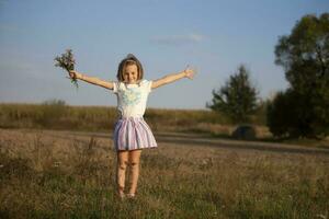 Beautiful little girl in the meadow with a bouquet of flowers. A child in a beautiful summer field. photo