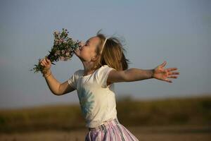 hermosa pequeño niña en el prado con un ramo de flores de flores un niño en un hermosa verano campo. foto