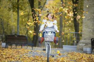 joven hermosa mujer paseos un bicicleta en un otoño parque debajo que cae hojas. foto