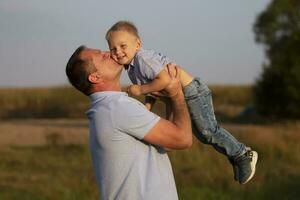 contento papá obras de teatro con su hijo en el antecedentes de el campo. alegre abuelo Besos su nieto. foto