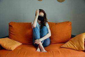 pretty woman wearing a mask sits on an orange sofa at home stay home concept photo