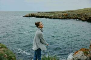 woman in a gray sweater stands on a rocky shore nature Lifestyle photo