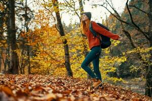 woman traveler with backpack walking in the park in autumn in nature side view photo