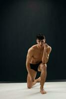 sporty man in black shorts kneels on a dark background photo