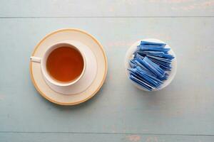 Paquete de edulcorante sustituto del azúcar y taza de té sobre fondo blanco. foto