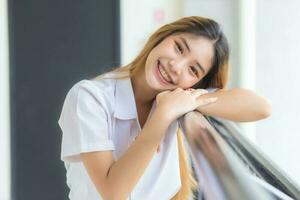 Beautiful and pretty young Asian girl student in Thai university student uniform smiling confidently and looking at camera in university background photo