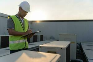 Asian maintenance engineer works on the roof of factory. contractor inspect compressor system and plans installation of air condition systems in construction. Checklist, inspector, control photo