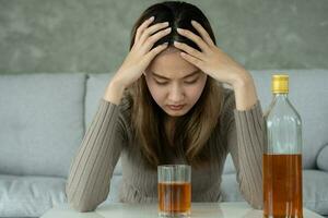 Deprimido joven asiático mujer fanático sensación malo Bebiendo whisky solo a hogar, estresado frustrado solitario Bebiendo alcohol sufre desde problemático espíritu, alcoholismo, vida y familia problemas foto