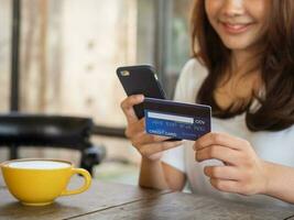 el sonriente joven asiático mujer disfruta compras en línea vía un teléfono inteligente y pago en línea vía crédito tarjeta. conveniencia de gasto sin dinero en efectivo. foto