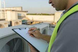 Asian maintenance engineer works on the roof of factory. contractor inspect compressor system and plans installation of air condition systems in construction. Checklist, inspector, control photo