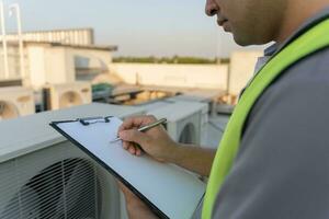 asiático mantenimiento ingeniero trabajos en el techo de fábrica. contratista inspeccionar compresor sistema y planes instalación de aire condición sistemas en construcción. Lista de Verificación, inspector, controlar foto