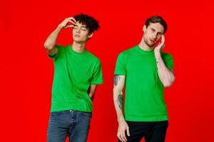 two friends in green t-shirts are standing next to tin with their hands emotions red background photo