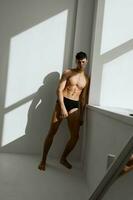 athletic male bodybuilder in black shorts posing near the window photo