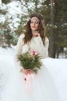 Beautiful bride in a white dress with a bouquet in a snow-covered winter forest. Portrait of the bride in nature. photo