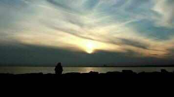 Man watching view at sunset, man walking over rocky and jumping towards seaside, selective focus video