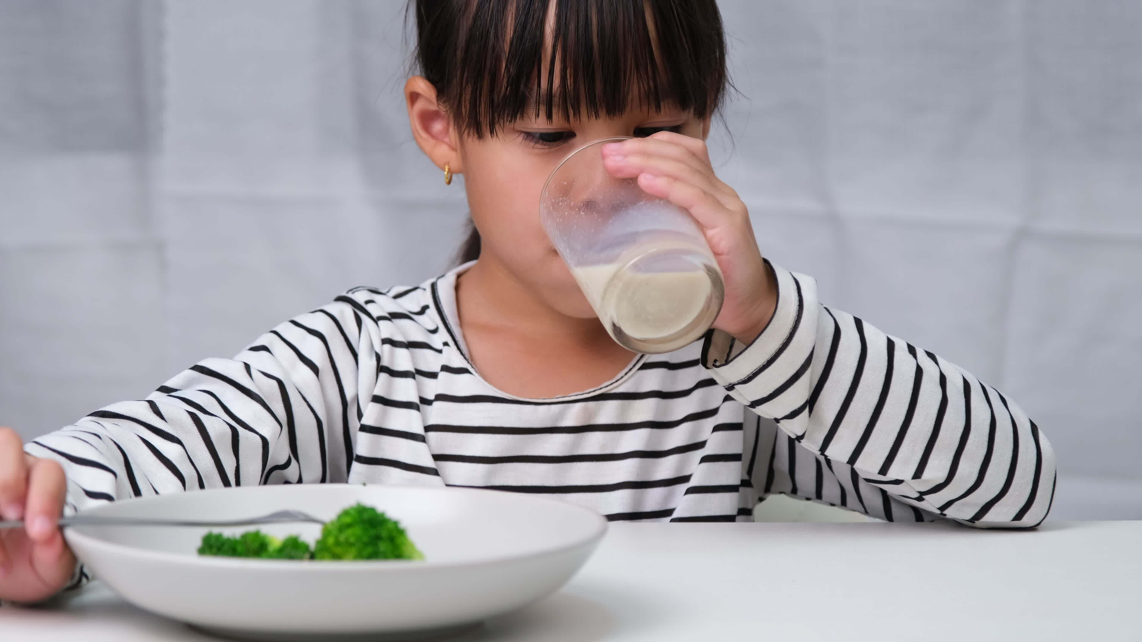 Cute Asian girl drinking a glass of milk in the morning before going to