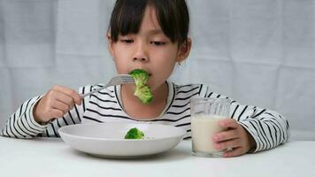 söt asiatisk flicka dricka en glas av mjölk i de morgon- innan gående till skola. liten flicka äter friska grönsaker och mjölk för henne måltider. friska mat i barndom. video