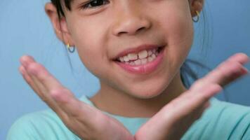 avvicinamento di sorridente giovane ragazza rivelatrice sua bellissimo bianca denti su un' blu sfondo. concetto di bene Salute nel infanzia. video