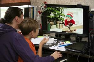 The woman and the child are sitting at the table and talking via video link with the boy on the computer. Staying at home, quarantine and social distancing during the New Years. photo