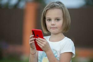 Child with a smartphone. Funny little girl with a red phone. photo