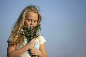 hermosa pequeño niña con un ramo de flores de salvaje flores en contra el cielo. foto