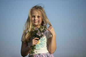 Beautiful little girl with a bouquet of wild flowers against the sky. photo