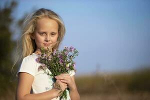 Beautiful little girl with a bouquet of wild flowers against the sky. photo