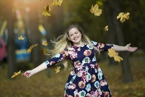 A beautiful girl in an autumn park scatters maple leaves. photo