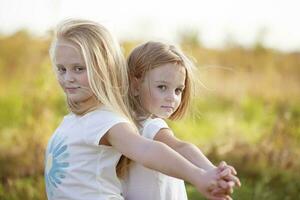 Two little girls stand with their backs to each other with their hands up in the field. Sisters. photo