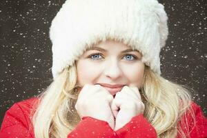 retrato de un hermosa rubia niña en un calentar sombrero y que cae nieve. foto
