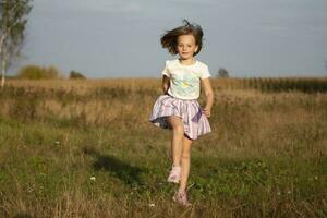 hermosa pequeño niña carreras en el verano campo. el niño obras de teatro en el prado. foto