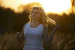 un hermosa de edad mediana mujer son caminando en el campo en contra el antecedentes de puesta de sol. foto