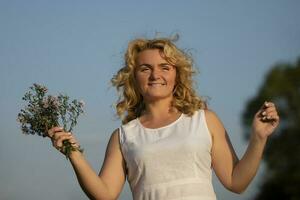 hermosa de edad mediana rubia con un ramo de flores de flores silvestres en contra el azul cielo. foto