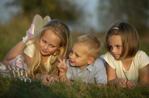 hermanas y pequeño hermano mentira en el césped. niños jugar en el prado. un contento familia. foto