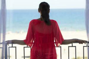 A middle-aged woman stands on a balcony overlooking the sea. photo