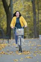 contento medio Envejecido mujer paseos un bicicleta en el otoño parque. foto