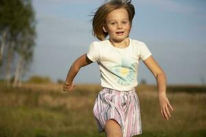 Beautiful little girl runs in the summer field. The child plays in the meadow. photo