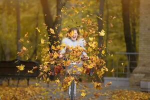 joven hermosa mujer paseos un bicicleta en un otoño parque debajo que cae hojas. foto
