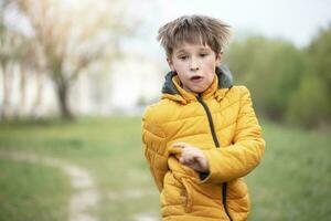 A child in a yellow jacket runs against the backdrop of greenery. photo