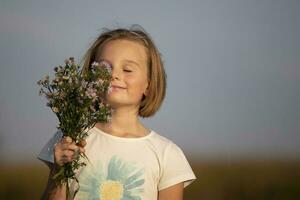 Beautiful little girl with a bouquet of meadow flowers. A child in a beautiful summer field. photo